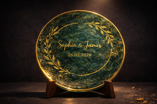 Personalized fused glass wedding plate with gold lettering showing the names Louise and Jakob and the date 12 May 2020, displayed on a wooden stand with candles and flowers.